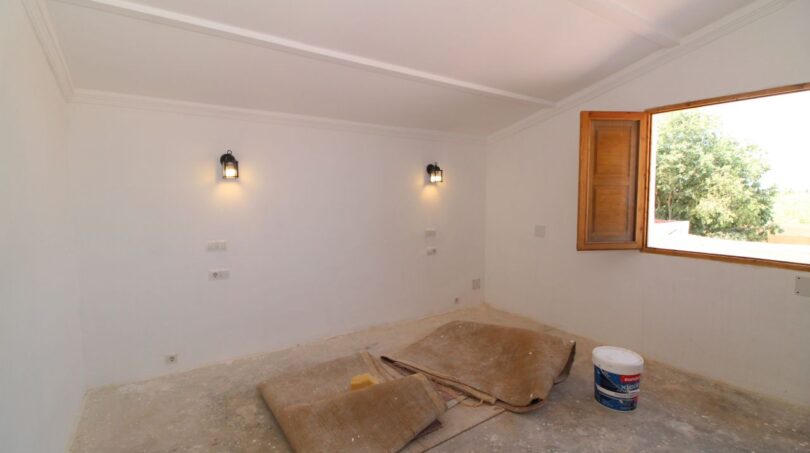 Renovierungsbedürftiges Zimmer der Finca in Son Ferriol mit Wandleuchten und Holzfenster zum Garten