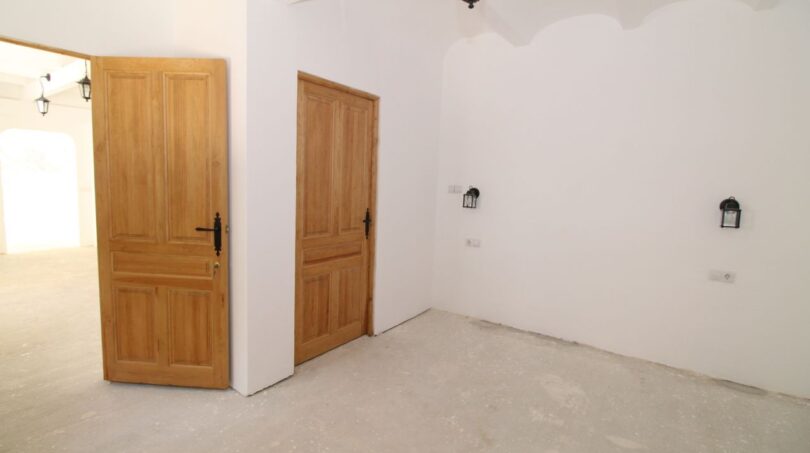 Heller Eingangsbereich der Finca mit rustikalen Holztüren, weißen Wänden und traditionellen Wandleuchten.