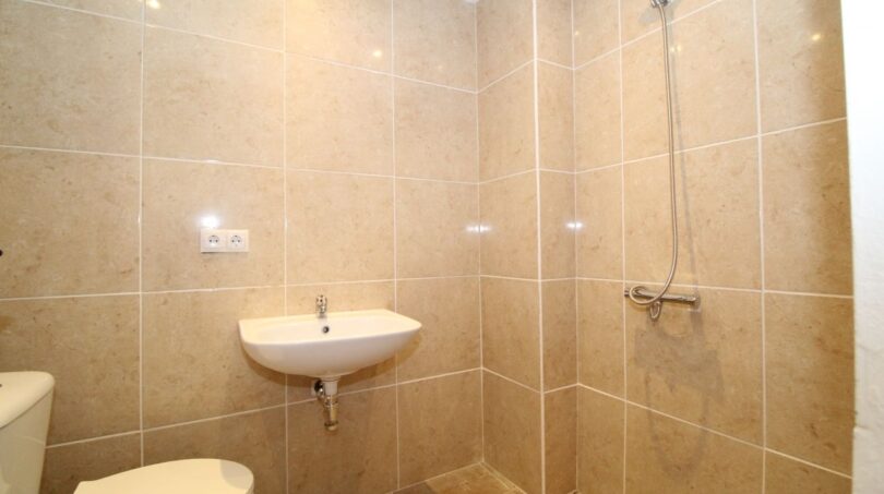 Helles Badezimmer der Finca mit beigen Marmorfliesen, Dusche, Waschbecken und WC.