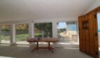 Heller Wintergarten der Finca mit Panoramafenstern, Holztisch und Blick auf Garten und Pool