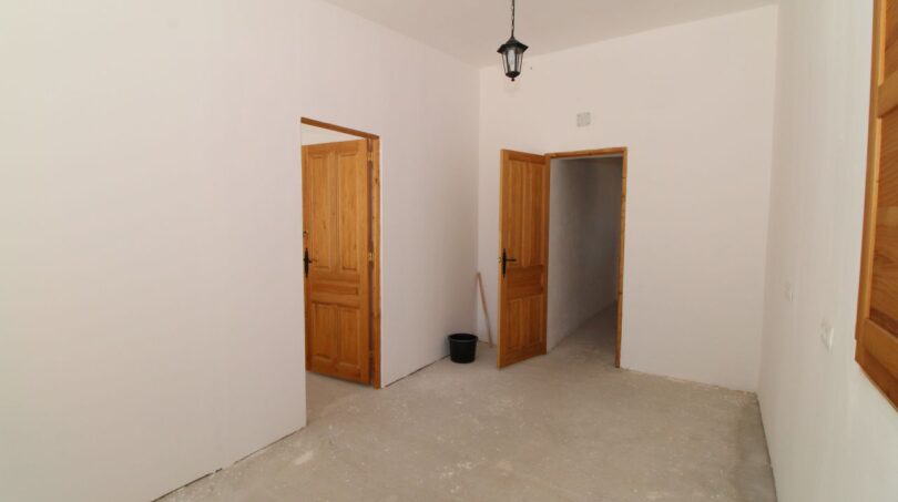 Leerer Zimmer der Finca in Son Ferriol mit zwei Holztüren, weißen Wänden und Betonboden.