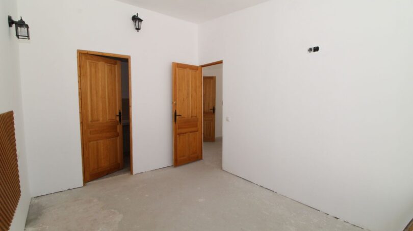 Leeres Zimmer der Finca mit zwei Holztüren, weißen Wänden und Betonboden in Son Ferriol