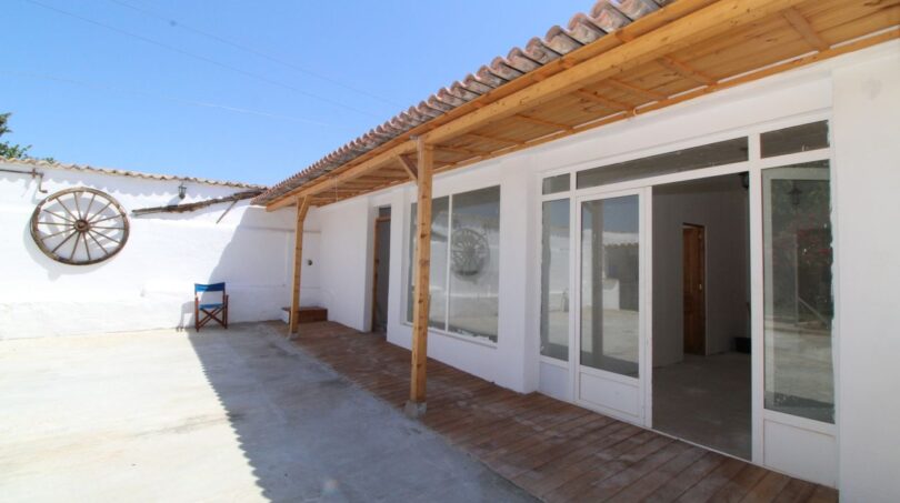 Überdachte Terrasse der Finca in Son Ferriol mit Holzbalken, Terrakottafliesen und großen Glastüren zum Innenbereich.