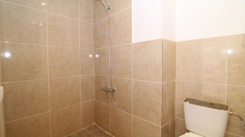 Gefliestes Duschbad der Finca in Son Ferriol mit bodenebener Dusche und WC, beige Marmoroptik-Fliesen.