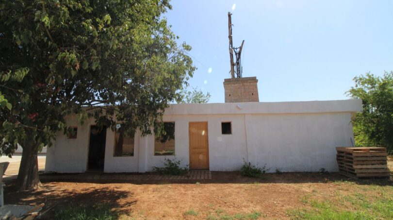 Außenansicht der Finca in Son Ferriol mit weißer Fassade, Windmühlenturm und Baumbewuchs.