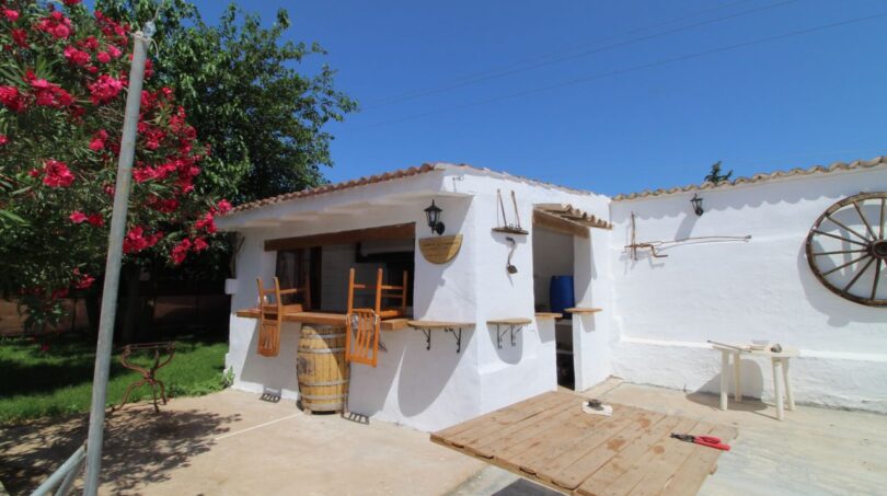 Rustikale Außenterrasse der Finca Son Ferriol mit weißer Fassade, Holztisch, Weinfass und dekorativem Wagenrad.