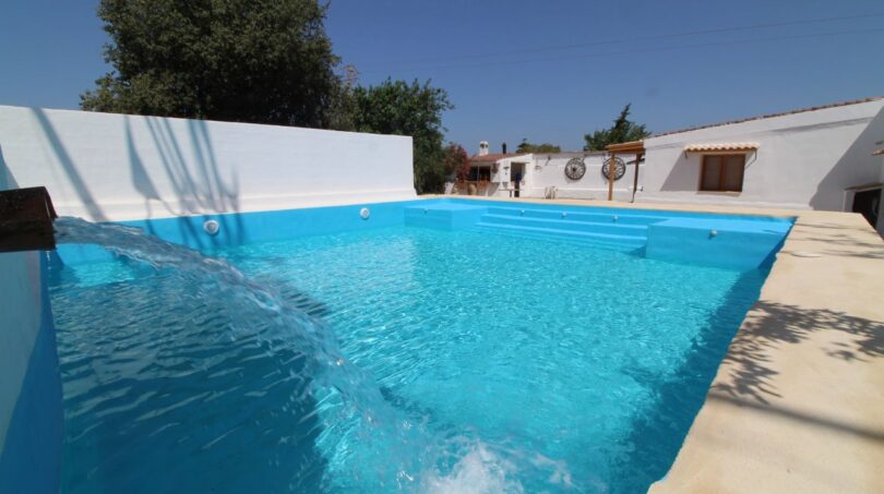 Großer Pool mit Wasserfall der Finca in Son Ferriol, umgeben von weißen Mauern und mediterranem Garten.