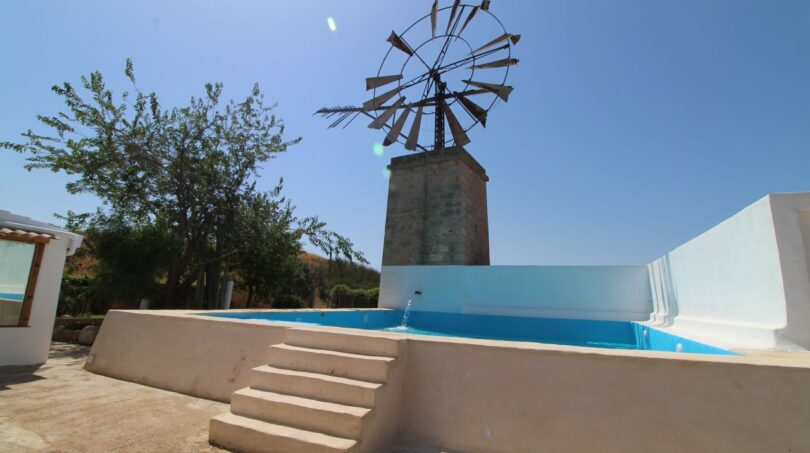 Außenbereich der Finca mit blauem Pool, historischer Windmühle auf Steinturm und Naturlandschaft in Son Ferriol.