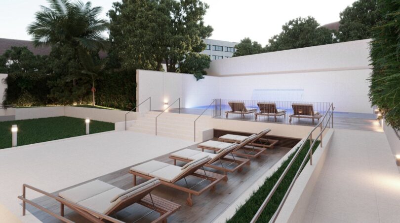 Modern pool terrace with wooden loungers, white stone walls and tropical plants in Palma de Mallorca