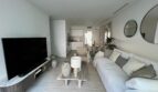 Helles Wohnzimmer mit weißem Sofa, großem TV und offener Küche in modernem Luxus-Apartment in Palma de Mallorca.