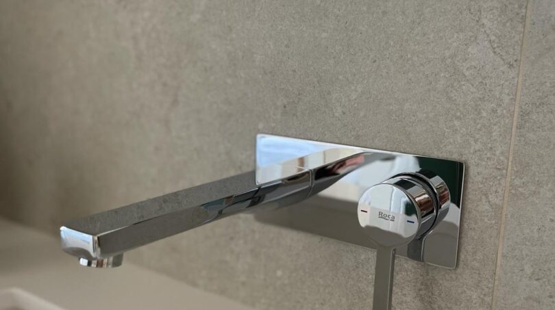 Elegante Wandarmatur von Roca in Chrom an grauer Natursteinwand über weißem Waschbecken im Luxus-Apartment Palma