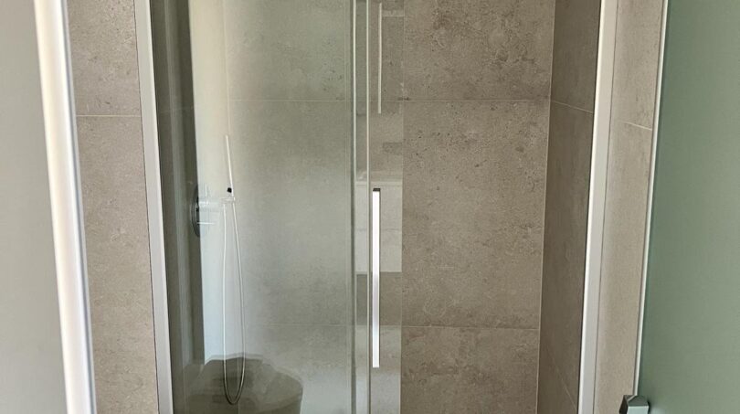 Modernes Duschbad mit Glasschiebtür, Regendusche und eleganten Beigefliesen im Luxusapartment Palma