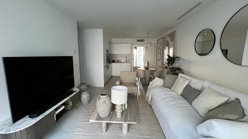 Helles Wohnzimmer mit weißem Sofa, großem TV und offener Küche im Luxusapartment Palma de Mallorca