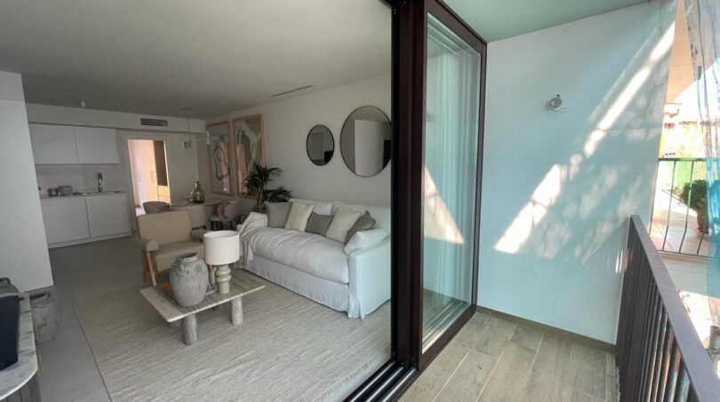 Balkon mit Glasschiebetür zum hellen Wohnzimmer, weißem Sofa und moderner Einrichtung in Luxusapartment Palma
