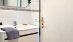 Modernes weißes Badezimmer mit Waschtischunterschrank, Rundspiegel und dekorativer Pflanze in Strandwohnung Palma