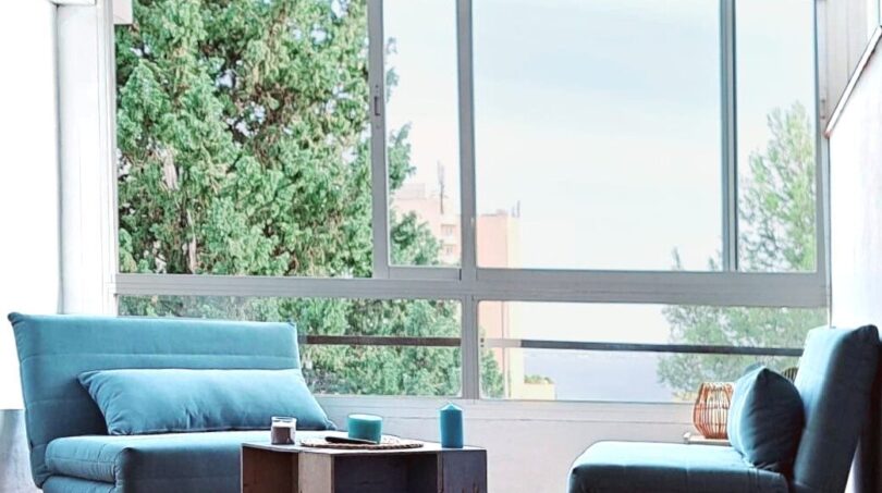 Helles Wohnzimmer mit türkisfarbenen Sofas, Panoramafenstern und Blick auf Palmen in Palma de Mallorca.