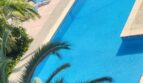 Rechteckiger Außenpool mit türkisblauem Wasser, Sonnenliegen und Palmen in Wohnanlage nahe dem Strand in Palma de Mallorca.