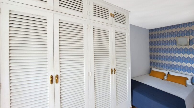 Schlafzimmer mit weißem Einbauschrank, blauer Bettwäsche und gemusterter Tapete in Strandwohnung Palma de Mallorca