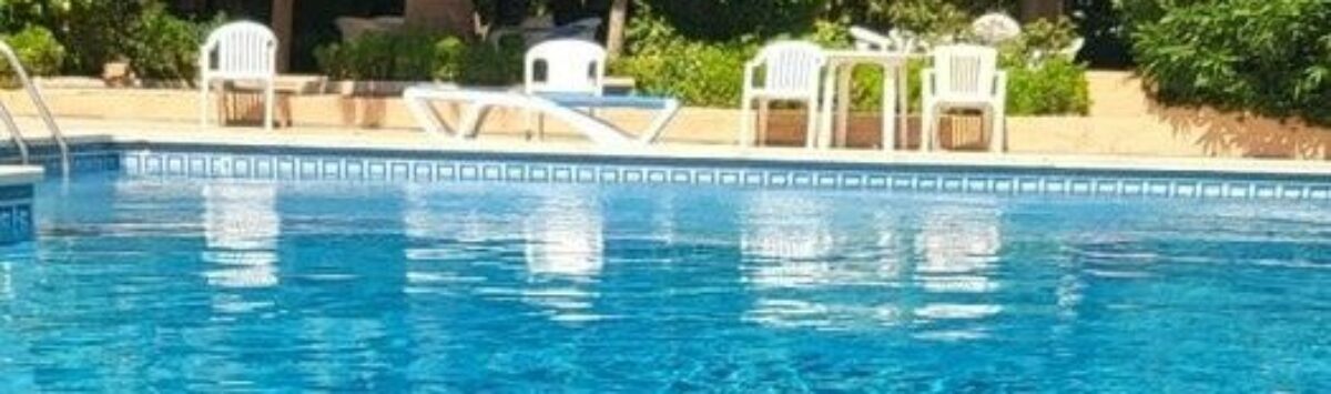 Hotel pool with turquoise blue water, palm trees and white sun loungers in Palma de Mallorca
