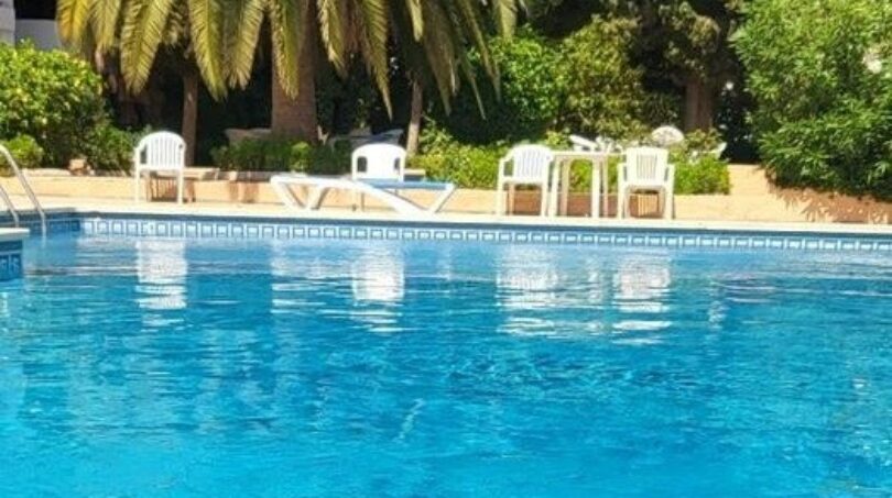 Hotel pool with turquoise blue water, palm trees and white sun loungers in Palma de Mallorca