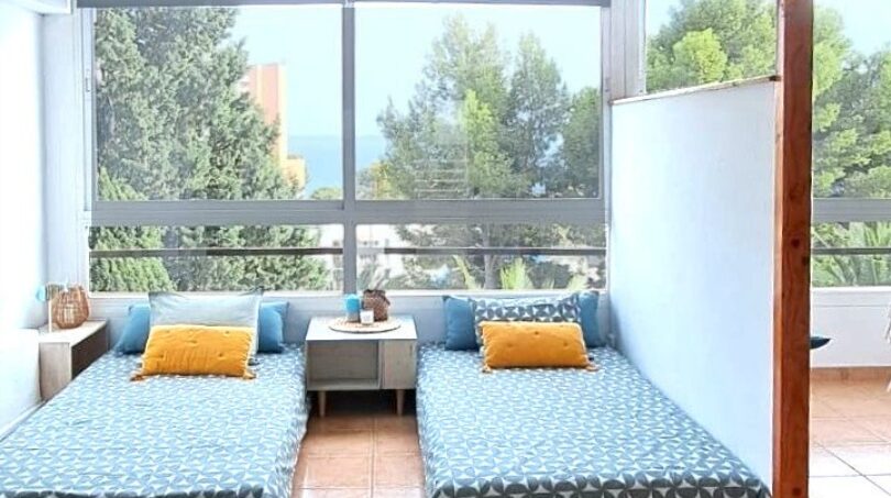 Helles Schlafzimmer mit zwei Einzelbetten, blauen Tagesdecken und Panoramafenster mit Meerblick in Palma