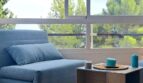 Heller Wohnbereich mit blauem Sessel, Beistelltisch und großer Fensterfront mit Grünblick in Palma de Mallorca