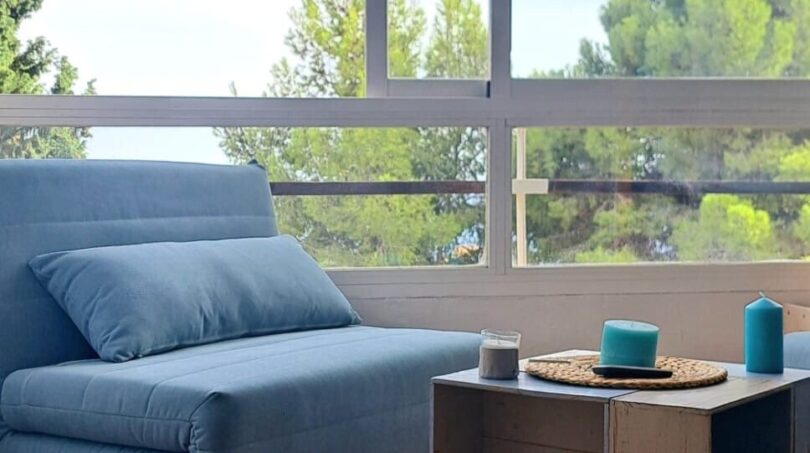 Heller Wohnbereich mit blauem Sessel, Beistelltisch und großer Fensterfront mit Grünblick in Palma de Mallorca