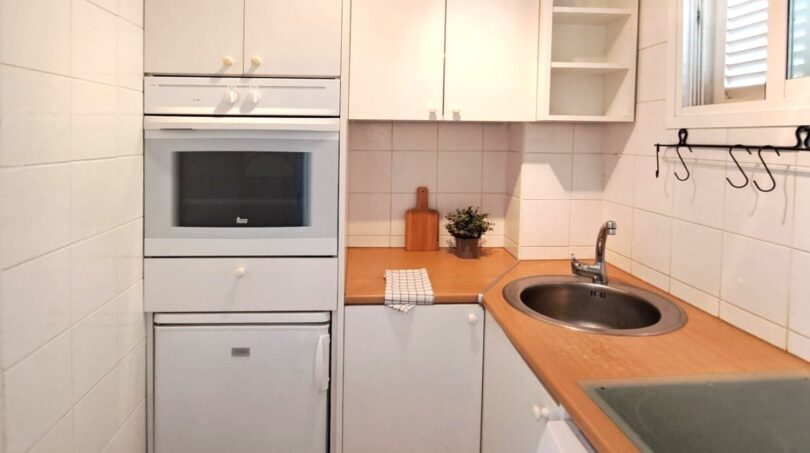 Kompakte weiße Küche mit Einbauofen, Mikrowelle, Rundspüle und Waschmaschine in strandnaher Wohnung in Palma de Mallorca.