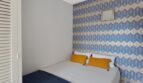 Helles Schlafzimmer mit Doppelbett, blauer Tagesdecke, gelben Kissen und dekorativem Tapetenwandmuster in Strandwohnung Palma.