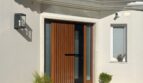 Área de entrada moderna de una villa en Santa Ponça con puerta de madera, costados de cristal y ambiente mediterráneo.