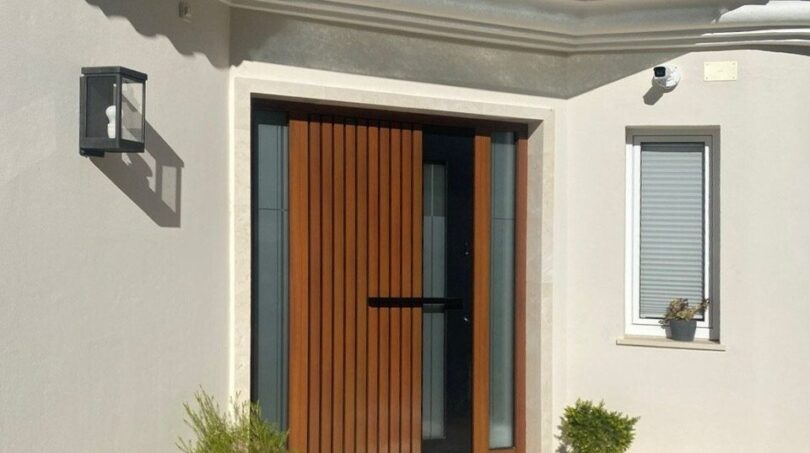 Área de entrada moderna de una villa en Santa Ponça con puerta de madera, costados de cristal y ambiente mediterráneo.