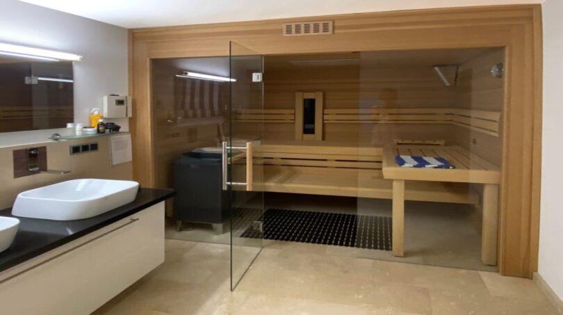 Baño de lujo de la villa en Santa Ponça con sauna de madera integrada, frente de cristal y elegantes baldosas de mármol.