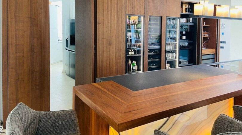 Moderna cocina-salón de la villa en Santa Ponça con barra de madera, barra iluminada y elegantes armarios para vino.