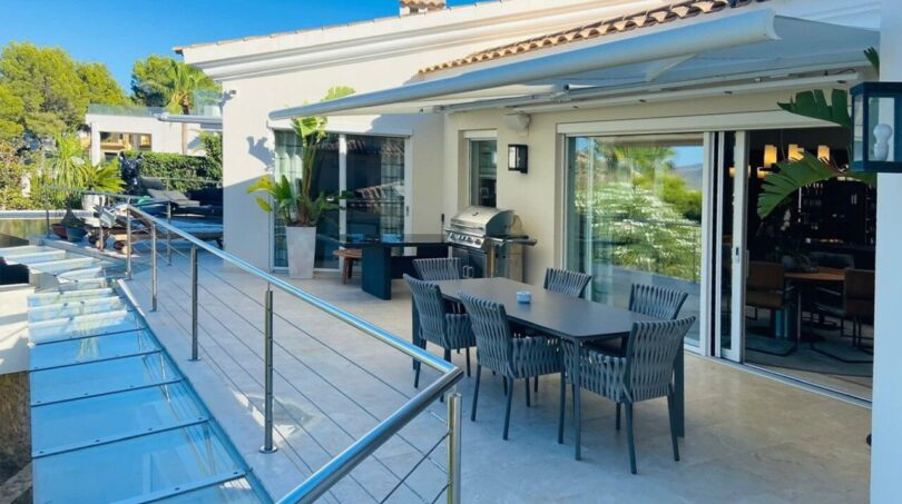 Moderna terraza de la villa en Santa Ponça con área de comedor al aire libre, toldo y barandilla de cristal.