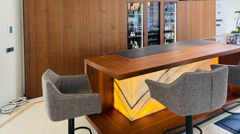 Elegante barra de casa con revestimiento de ónix iluminado, revestimiento de madera y enfriador de vino en villa moderna, Santa Ponça.