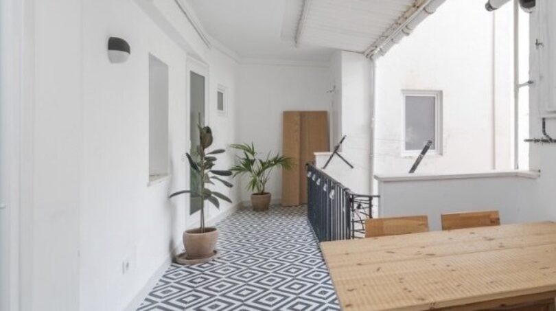 Überdachte Terrasse mit geometrischem Zementfliesenboden, Holztisch und Stühlen, Pflanzen, weißen Wänden in Palma.