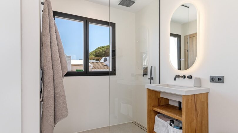 Modernes Badezimmer der Villa mit Glasdusche, Holzwaschtisch und beleuchtetem Spiegel in Sol de Mallorca