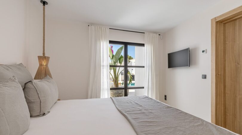 Helles Schlafzimmer der Traumvilla in Sol de Mallorca mit Doppelbett, Pendellampe und Terrassenzugang zum Pool.