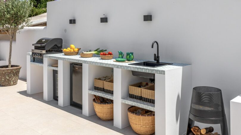 Moderne Außenküche der Traumvilla mit Grill, Spüle, Weidenkorb-Stauraum und mediterranem Flair.