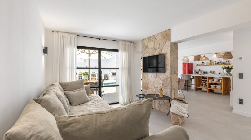 Helles Wohnzimmer der Villa mit Natursteinwand, TV, Sofa und Zugang zur Poolterrasse in Sol de Mallorca
