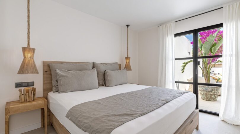 Helles Schlafzimmer der Traumvilla in Sol de Mallorca mit Doppelbett, Holzmöbeln und Balkon mit Bougainvillea.