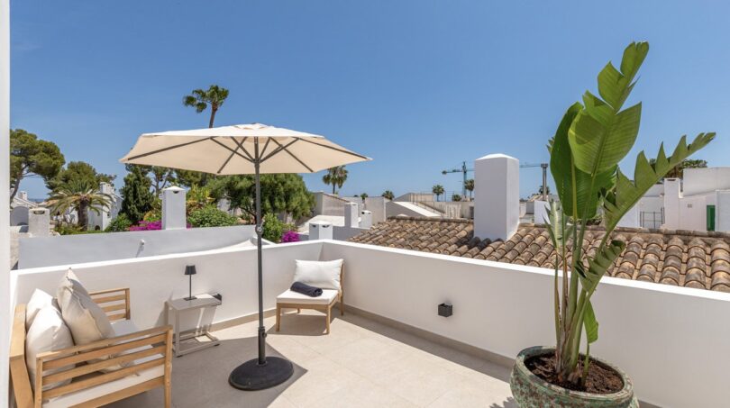 Sonnige Dachterrasse der Villa in Sol de Mallorca mit Loungemöbeln, Sonnenschirm und Palmen