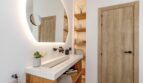 Modernes Badezimmer der Mallorca-Villa mit beleuchtetem Rundspiegel, Holzelementen und elegantem Waschtisch