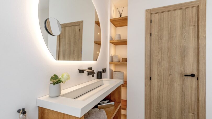 Modernes Badezimmer der Mallorca-Villa mit beleuchtetem Rundspiegel, Holzelementen und elegantem Waschtisch