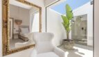 Helles Ankleidezimmer der Mallorca-Villa mit Goldrahmen-Spiegel, Bouclé-Sessel und tropischer Pflanze