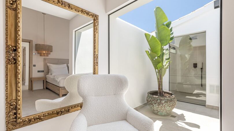 Helles Ankleidezimmer der Mallorca-Villa mit Goldrahmen-Spiegel, Bouclé-Sessel und tropischer Pflanze