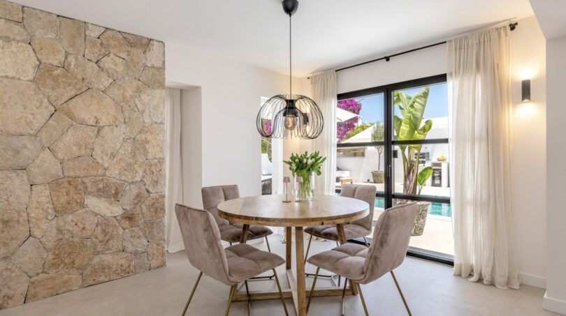 Elegantes Esszimmer der Traumvilla in Sol de Mallorca mit Natursteinwand, Rundtisch und Poolblick.