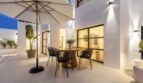 Beleuchtete Abendterrasse der Traumvilla in Sol de Mallorca mit rundem Holztisch, Korbstühlen und Sonnenschirm