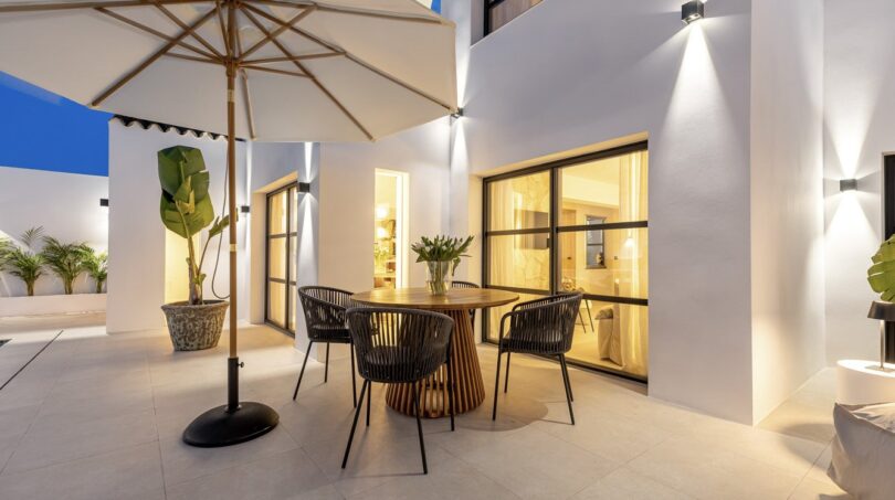 Beleuchtete Abendterrasse der Traumvilla in Sol de Mallorca mit rundem Holztisch, Korbstühlen und Sonnenschirm