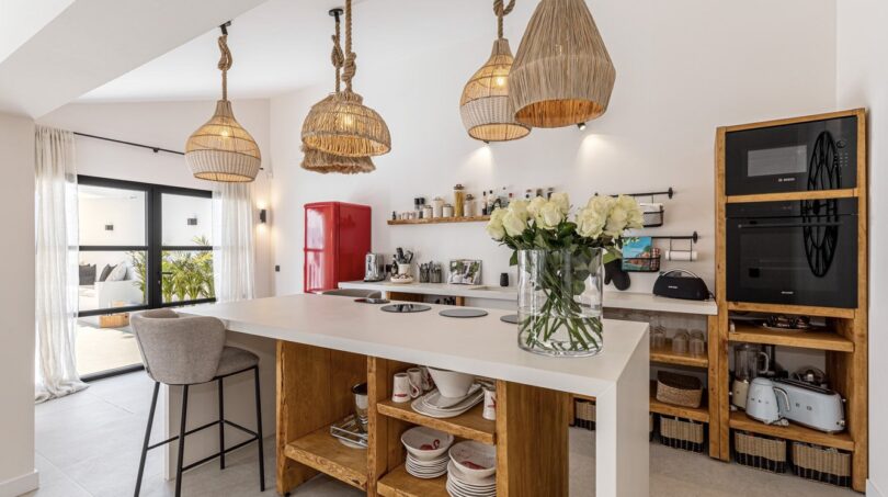 Moderne Küche der Traumvilla mit Kochinsel, Holzregalen und Rattanlampen in Sol de Mallorca